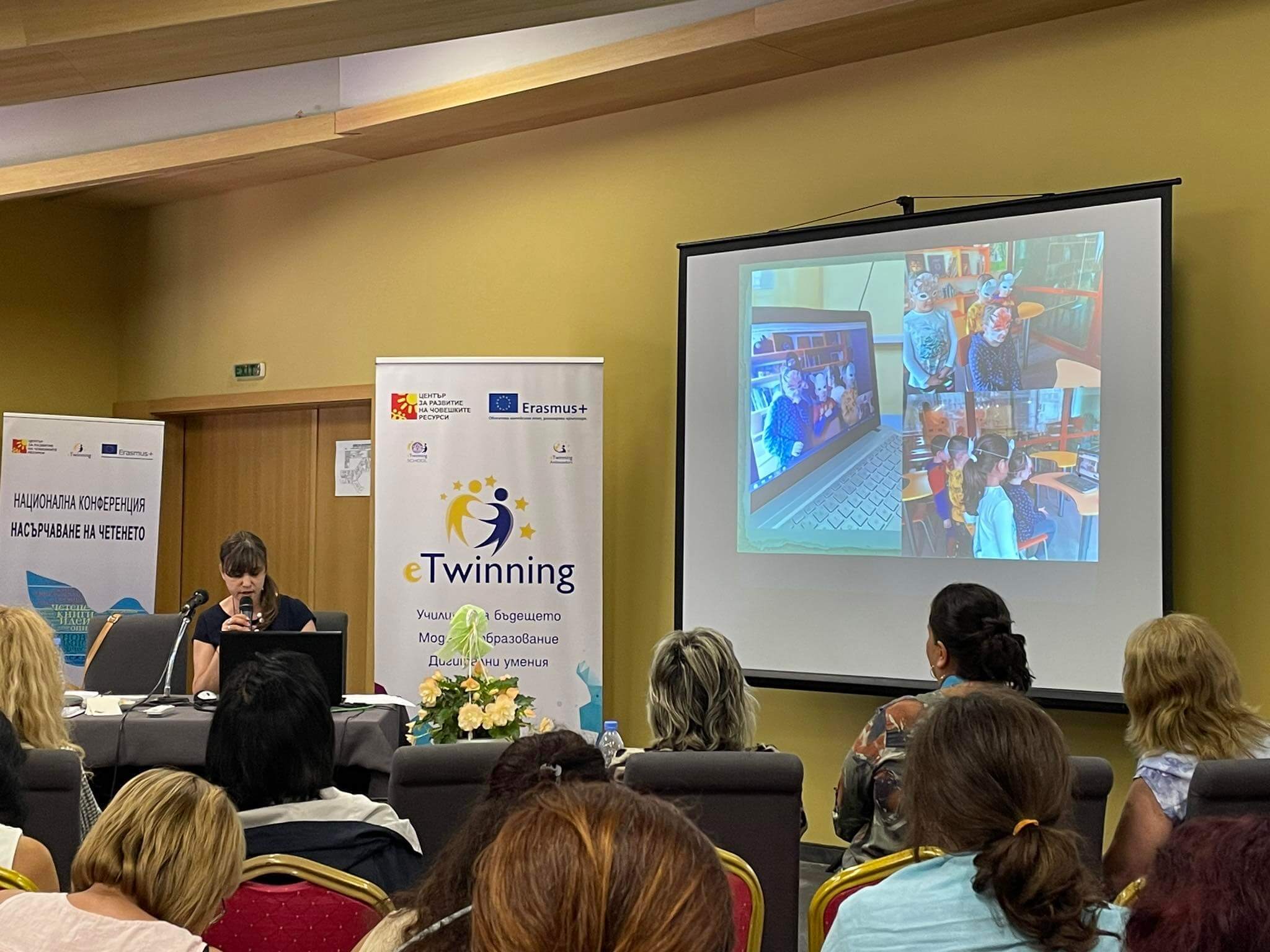 Конферентна зала. Мила изнася презентация. Публиката се вижда в гръб.