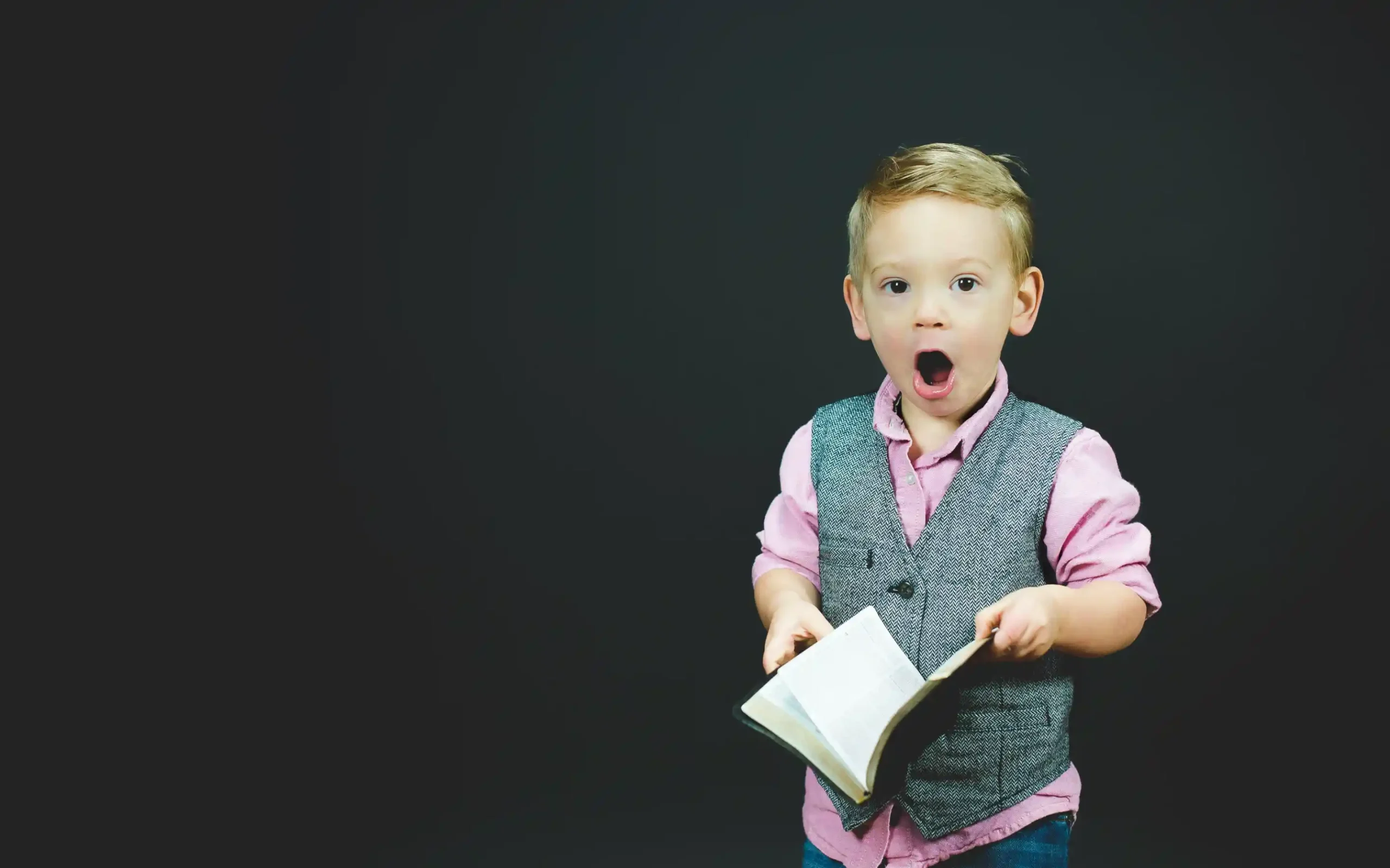 Малко момченце с книга в ръка гледа към камерата със забавна шокирана физиономия.