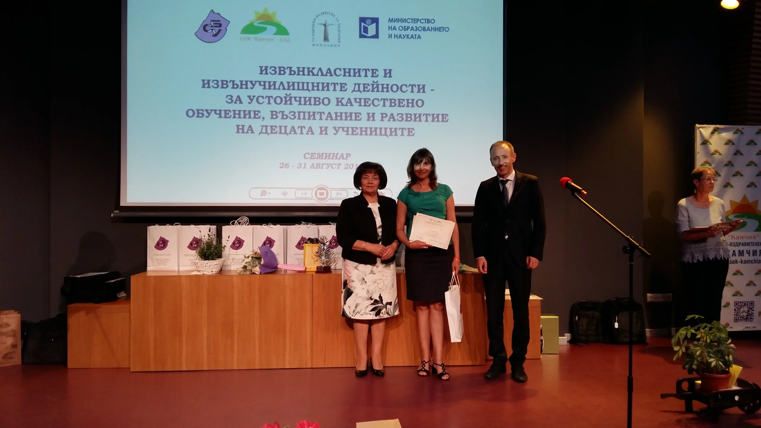 Мила Николова е застанала за снимка заедно с Янка Такева (председател на Синдиката на българските учители) и Красимир Вълчев (Министър на образованието). Връчват и грамота и награда.